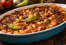 Καλοψημένα φασόλια μέσα σε ταψί με πλούσια κόκκινη σάλτσα, κομμάτια πράσου, καρότου και ολόκληρες καυτερές πιπεριές