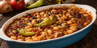 Καλοψημένα φασόλια μέσα σε ταψί με πλούσια κόκκινη σάλτσα, κομμάτια πράσου, καρότου και ολόκληρες καυτερές πιπεριές