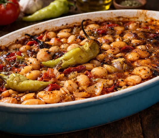 Καλοψημένα φασόλια μέσα σε ταψί με πλούσια κόκκινη σάλτσα, κομμάτια πράσου, καρότου και ολόκληρες καυτερές πιπεριές