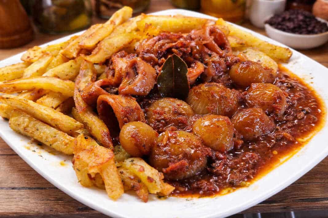 Καλαμαράκια στιφάδο σε πλούσια κόκκινη σάλτσα με κρεμμυδάκια κοκάρι δίπλα σε χρυσαφένιες τηγανητές πατάτες