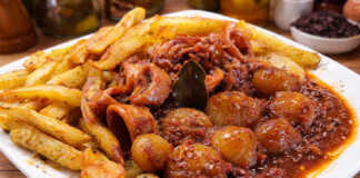 Καλαμαράκια στιφάδο σε πλούσια κόκκινη σάλτσα με κρεμμυδάκια κοκάρι δίπλα σε χρυσαφένιες τηγανητές πατάτες