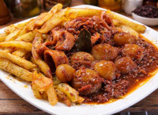 Καλαμαράκια στιφάδο σε πλούσια κόκκινη σάλτσα με κρεμμυδάκια κοκάρι δίπλα σε χρυσαφένιες τηγανητές πατάτες