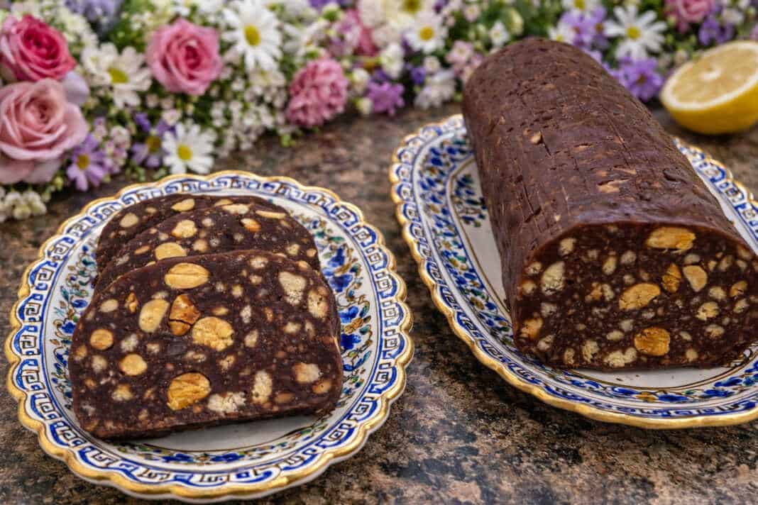 Λαχταριστές φέτες από σοκολατένιο κορμό με ολόκληρα κομμάτια μπισκότου και καρύδια σε ξύλινη επιφάνεια