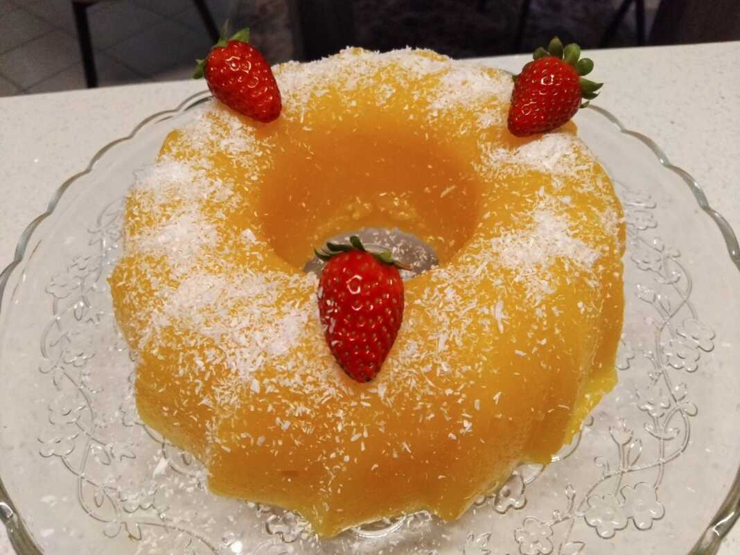 Ένα δροσερό πορτοκαλί γλυκό ψυγείου ξεφορμαρισμένο από φόρμα σιλικόνης πασπαλισμένο με λευκό ινδοκάρυδο στην κορυφή