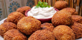 Ροδισμένοι, τραγανοί πατατοκεφτέδες σε πιατέλα, σερβιρισμένοι με ένα μπολάκι λευκή σως γιαουρτιού και φρέσκια ρίγανη