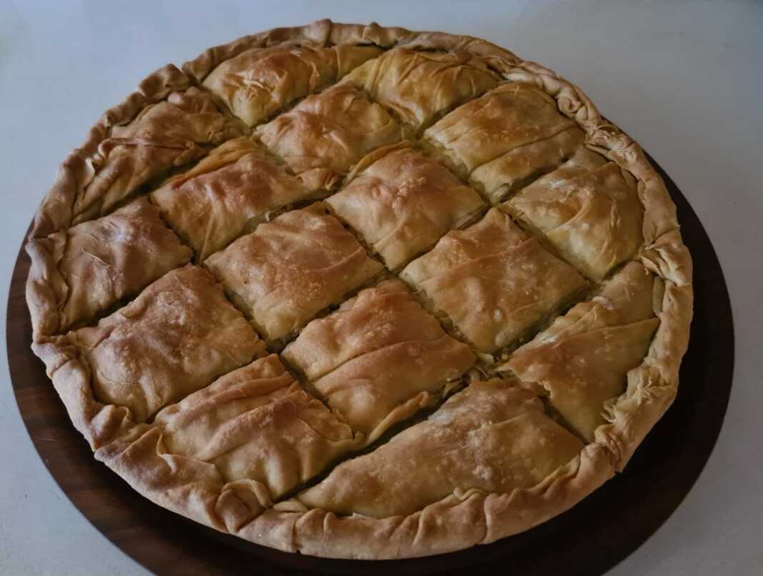 Μια μεγάλη στρογγυλή πρασοκιμαδόπιτα Μακεδονίας με χρυσαφένιο τραγανό φύλλο και πλούσιο κόθρο, κομμένη σε κομμάτια