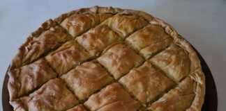 Μια μεγάλη στρογγυλή πρασοκιμαδόπιτα Μακεδονίας με χρυσαφένιο τραγανό φύλλο και πλούσιο κόθρο, κομμένη σε κομμάτια