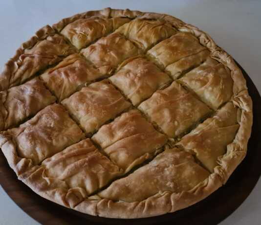 Μια μεγάλη στρογγυλή πρασοκιμαδόπιτα Μακεδονίας με χρυσαφένιο τραγανό φύλλο και πλούσιο κόθρο, κομμένη σε κομμάτια