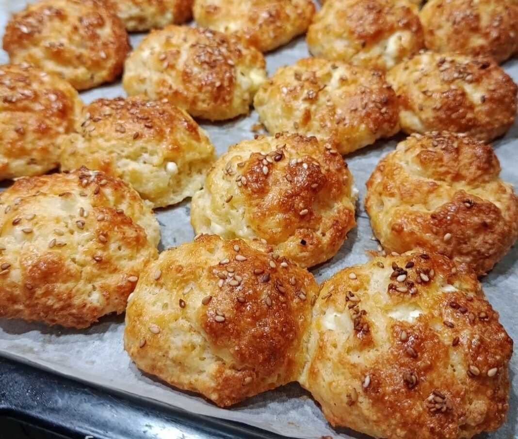 Μικρά ροδοκοκκινισμένα τυροπιτάκια πασπαλισμένα με σουσάμι πάνω σε λαδόκολλα, φρεσκοψημένα και αχνιστά