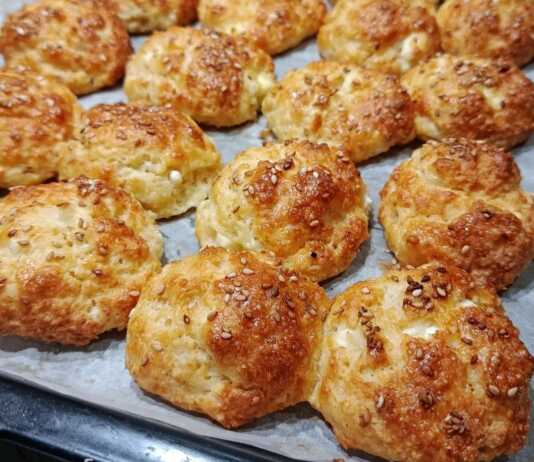 Μικρά ροδοκοκκινισμένα τυροπιτάκια πασπαλισμένα με σουσάμι πάνω σε λαδόκολλα, φρεσκοψημένα και αχνιστά