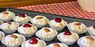 Αμυγδαλωτά: Η τέλεια συνταγή για μαστιχωτά και αρωματικά γλυκάκια Σειρές από λευκά αμυγδαλωτά πασπαλισμένα με άχνη ζάχαρη, διακοσμημένα με ολόκληρα αμύγδαλα και κόκκινα κεράσια πάνω σε λαδόκολλα.