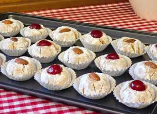 Αμυγδαλωτά: Η τέλεια συνταγή για μαστιχωτά και αρωματικά γλυκάκια Σειρές από λευκά αμυγδαλωτά πασπαλισμένα με άχνη ζάχαρη, διακοσμημένα με ολόκληρα αμύγδαλα και κόκκινα κεράσια πάνω σε λαδόκολλα.