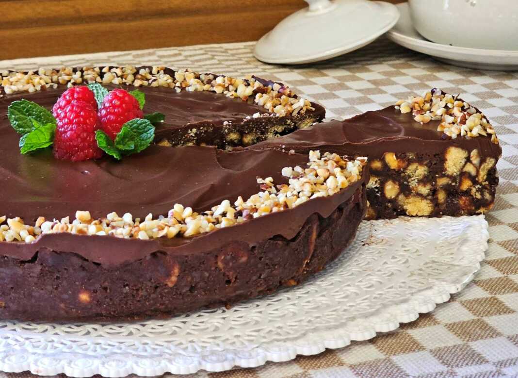 Ένα εντυπωσιακό σοκολατένιο γλυκό ψυγείου σε στρογγυλή φόρμα, καλυμμένο με γυαλιστερή γκανάζ σοκολάτας και διακοσμημένο με ολόκληρα καβουρδισμένα φουντούκια.