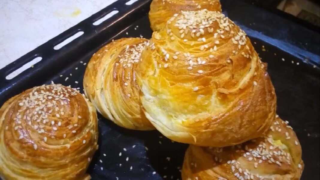 Μια πιατέλα με χρυσαφένια, στρογγυλά κρεατοπιτάκια, με ορατές τις λεπτές στρώσεις της ζύμης που θυμίζουν σφολιάτα, πασπαλισμένα με σουσάμι.