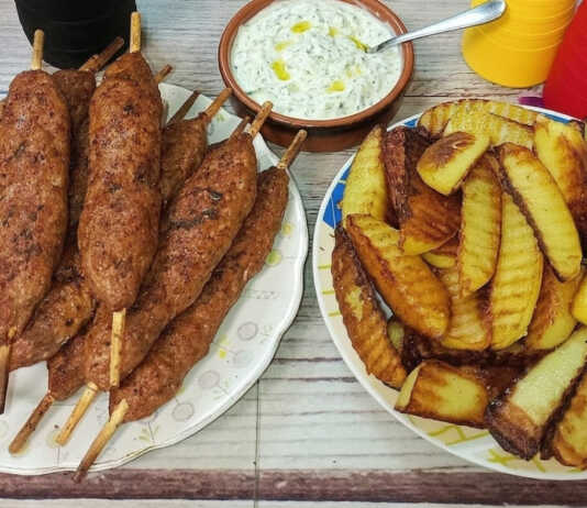 Ροδοκοκκινισμένα λουλά κεμπάπ σε ξυλάκια μέσα στο καλάθι του air fryer, σερβιρισμένα με δροσερό τζατζίκι.