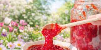 κατακόκκινη σπιτική μαρμελάδα φράουλα δίπλα σε φρέσκες ολόκληρες φράουλες και φέτες λεμονιού πάνω σε ξύλινη επιφάνεια.