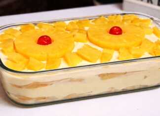 Ένα δροσερό γλυκό ψυγείου σε πυρέξ με στρώσεις σαβουαγιάρ, λευκή κρέμα και στολισμένο με ροδέλες ανανά και κόκκινα κερασάκια.