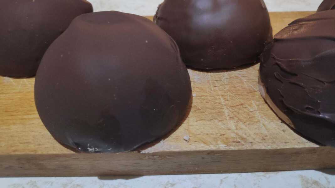 Σειρές από στρογγυλά τρουφάκια καλυμμένα με γυαλιστερή σοκολάτα, τοποθετημένα πάνω σε αντικολλητικό χαρτί.