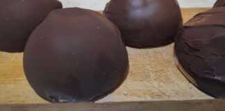 Σειρές από στρογγυλά τρουφάκια καλυμμένα με γυαλιστερή σοκολάτα, τοποθετημένα πάνω σε αντικολλητικό χαρτί.