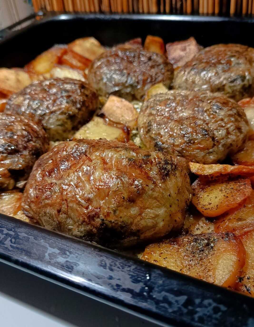 Ροδοκοκκινισμένοι τζιγεροσαρμάδες τυλιγμένοι σε μπόλια, τοποθετημένοι πάνω σε στρώση από προτηγανισμένες πατάτες μέσα στο ταψί.