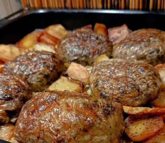 Ροδοκοκκινισμένοι τζιγεροσαρμάδες τυλιγμένοι σε μπόλια, τοποθετημένοι πάνω σε στρώση από προτηγανισμένες πατάτες μέσα στο ταψί.