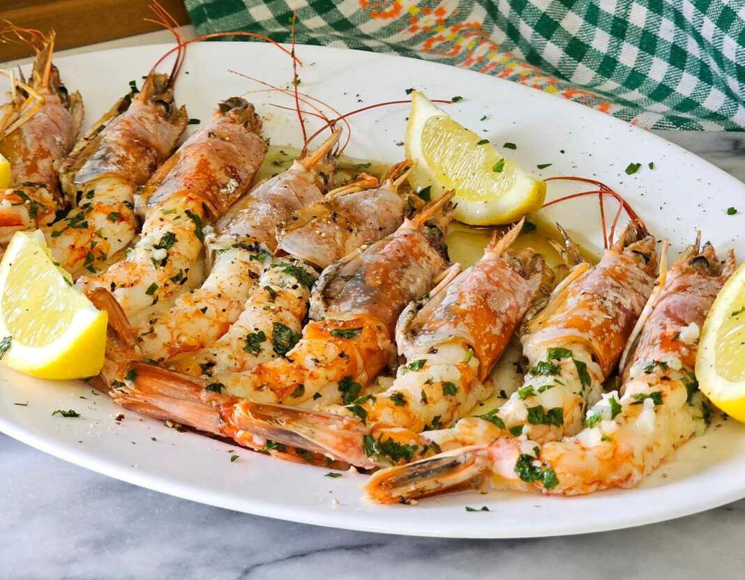Ζουμερές γαρίδες Αργεντινής ψημένες στο φούρνο, περιχυμένες με σάλτσα ελαιολάδου, λεμονιού και φρέσκου μαϊντανού μέσα σε ένα κεραμικό σκεύος.