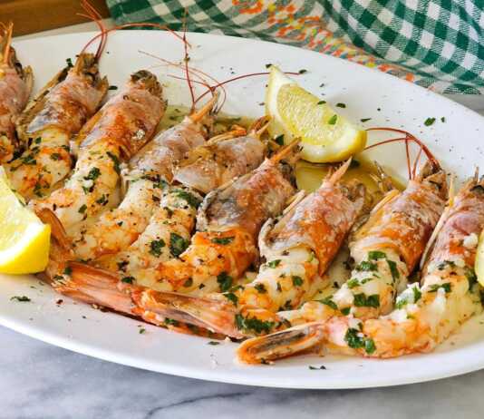 Ζουμερές γαρίδες Αργεντινής ψημένες στο φούρνο, περιχυμένες με σάλτσα ελαιολάδου, λεμονιού και φρέσκου μαϊντανού μέσα σε ένα κεραμικό σκεύος.