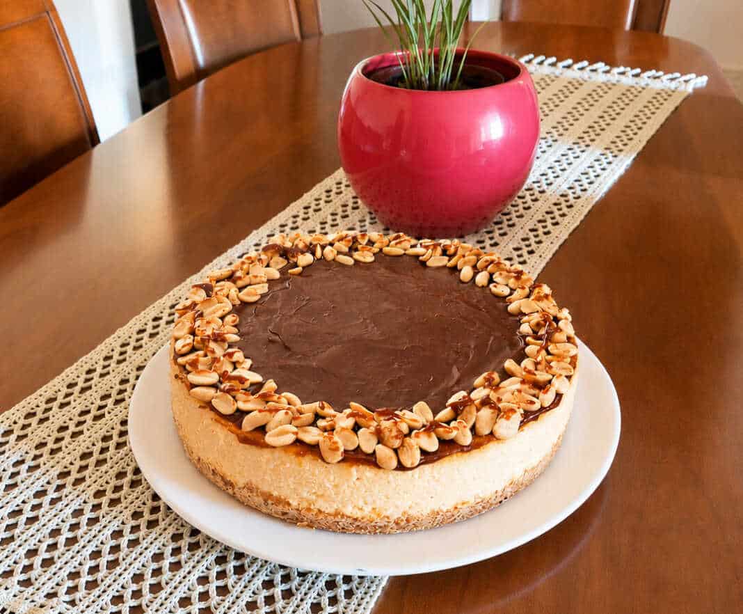 Λαχταριστό και βελουδένιο cheesecake φούρνου με πλούσια στρώση ρευστής καραμέλας βουτύρου και καβουρδισμένα φιστίκια στην κορυφή, κομμένο σε κομμάτι.