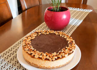 Λαχταριστό και βελουδένιο cheesecake φούρνου με πλούσια στρώση ρευστής καραμέλας βουτύρου και καβουρδισμένα φιστίκια στην κορυφή, κομμένο σε κομμάτι.