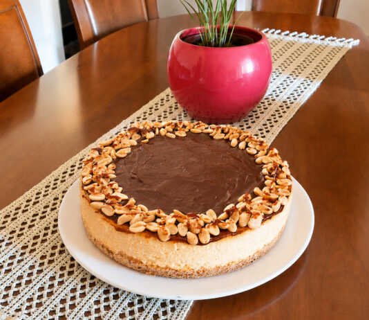 Λαχταριστό και βελουδένιο cheesecake φούρνου με πλούσια στρώση ρευστής καραμέλας βουτύρου και καβουρδισμένα φιστίκια στην κορυφή, κομμένο σε κομμάτι.