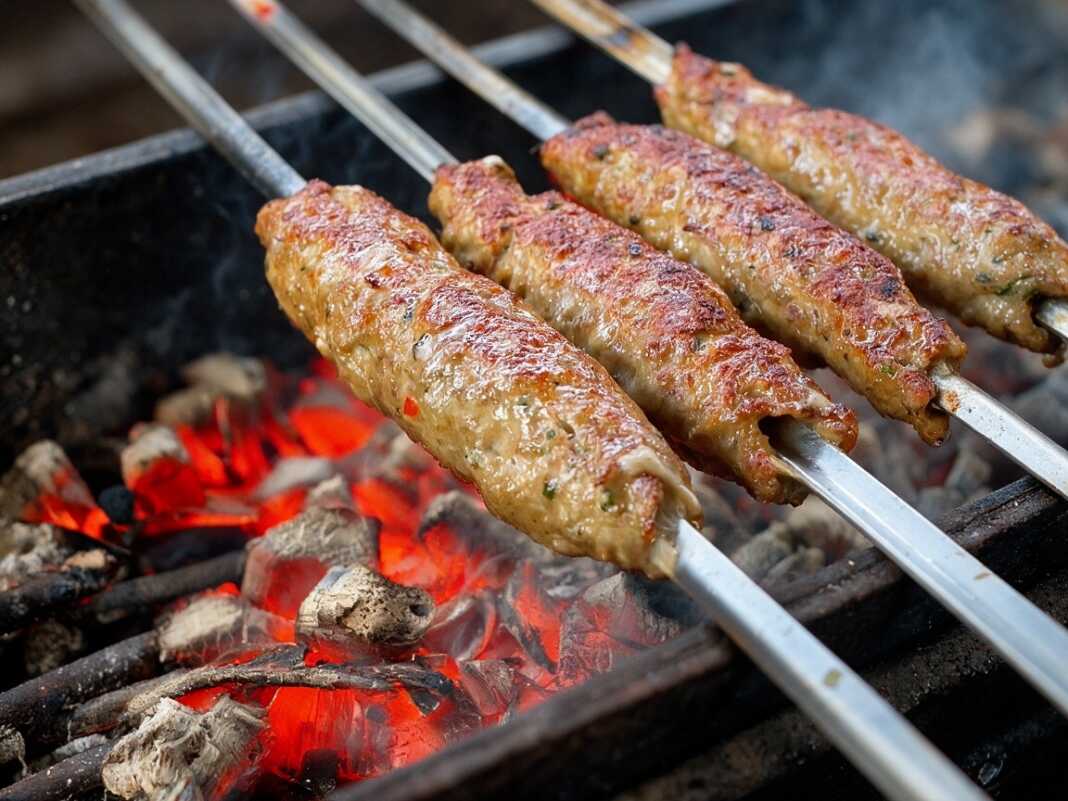 Πλατιές μεταλλικές σούβλες με ροδοκοκκινισμένα, ζουμερά κεμπαπ να ψήνονται πάνω από αναμμένα κάρβουναστην αυλή
