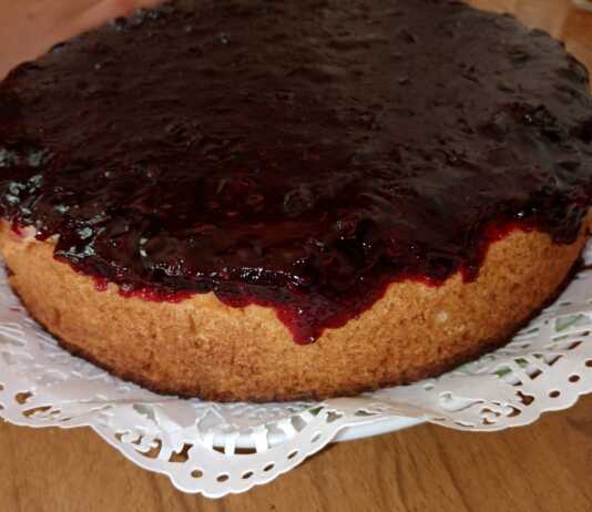 Ένα κομψό ψητό cheesecake σε πιατέλα, με μια πλούσια, λαμπερή κατακόκκινη σάλτσα από φράουλες και μούρα να απλώνεται ομοιόμορφα στην επιφάνειά του