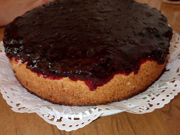 Ένα κομψό ψητό cheesecake σε πιατέλα, με μια πλούσια, λαμπερή κατακόκκινη σάλτσα από φράουλες και μούρα να απλώνεται ομοιόμορφα στην επιφάνειά του