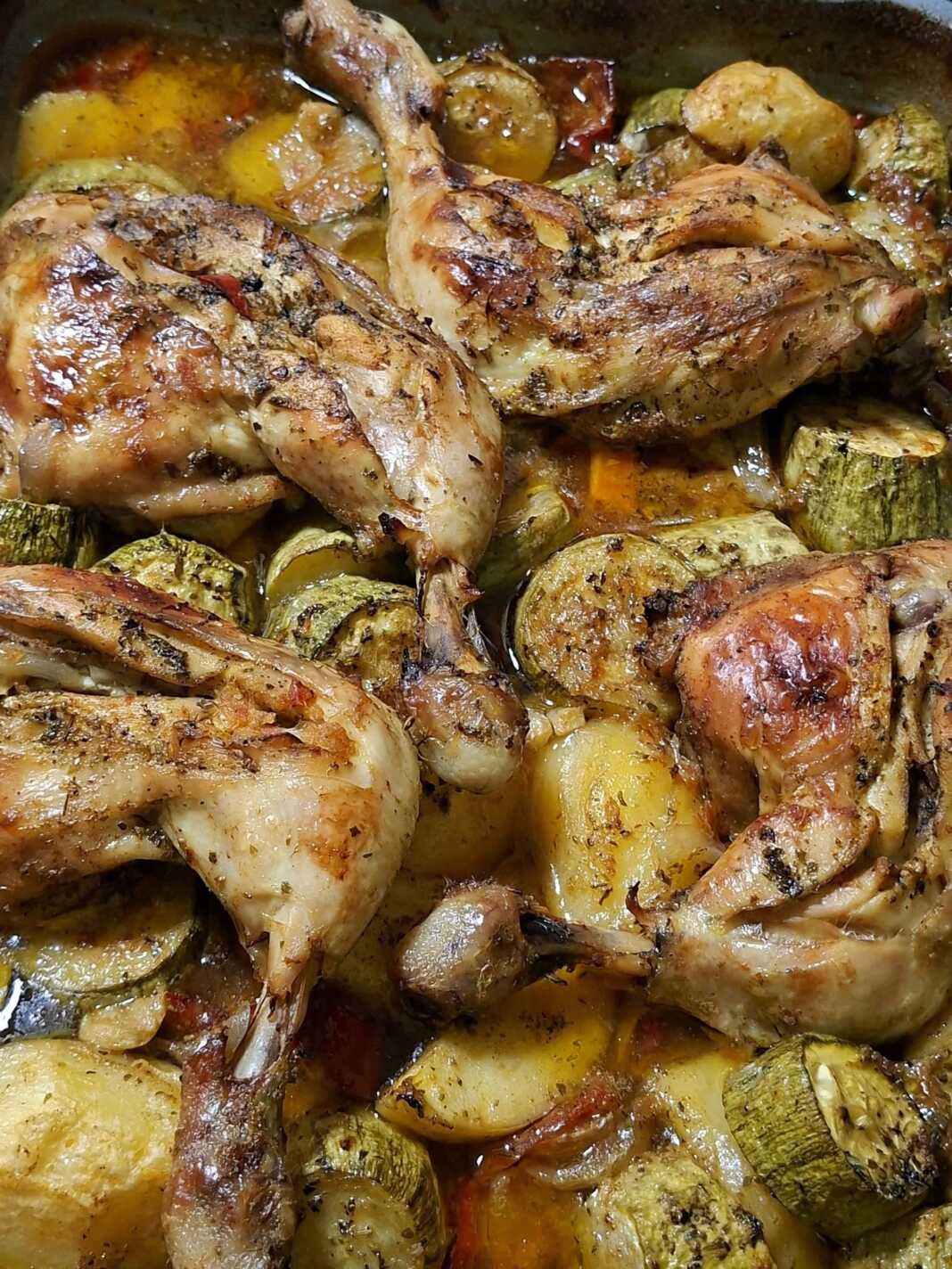 Ένα βαθύ ταψί με ροδοψημένα μπουτάκια κοτόπουλου πάνω από μια πλούσια στρώση από πατάτες, κολοκυθάκια και πιπεριές σε σάλτσα ντομάτας