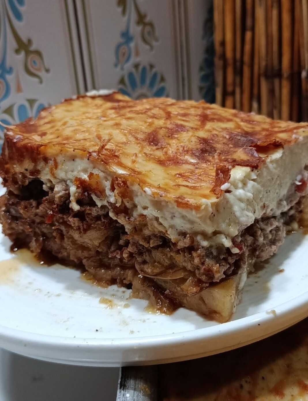 Ένα μεγάλο κομμάτο παραδοσιακό μουσακά, με μια ροδοψημένη, χρυσή κρούστα μπεσαμέλ στην επιφάνεια και εμφανείς τις στρώσεις λαχανικών και κιμά